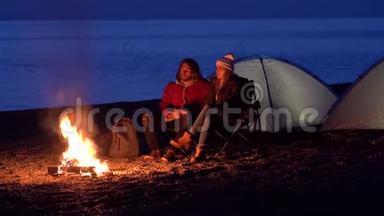 一对年轻夫妇坐在火炉旁。 在海边用帐篷露营。 <strong>春晚</strong>
